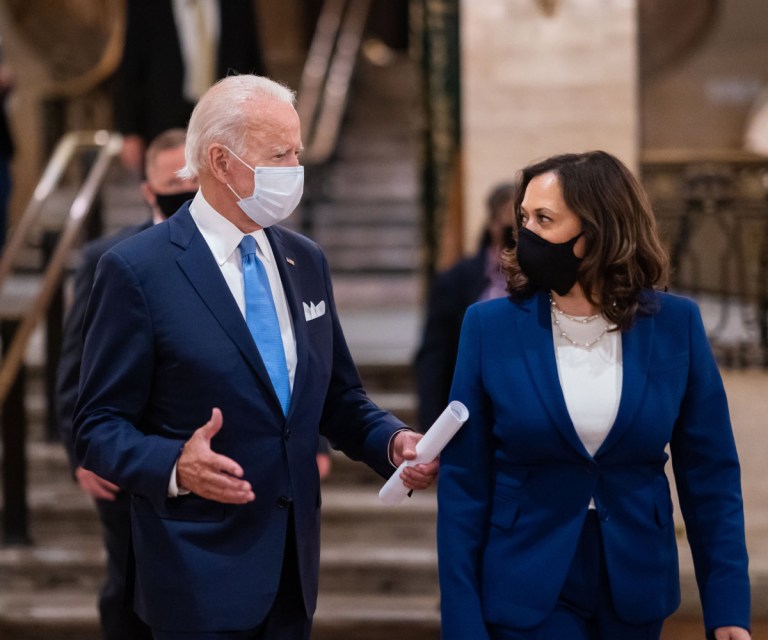 El presidente Biden y la vicepresidente Harris hablan entre ellos mientras usan máscaras y trajes azules