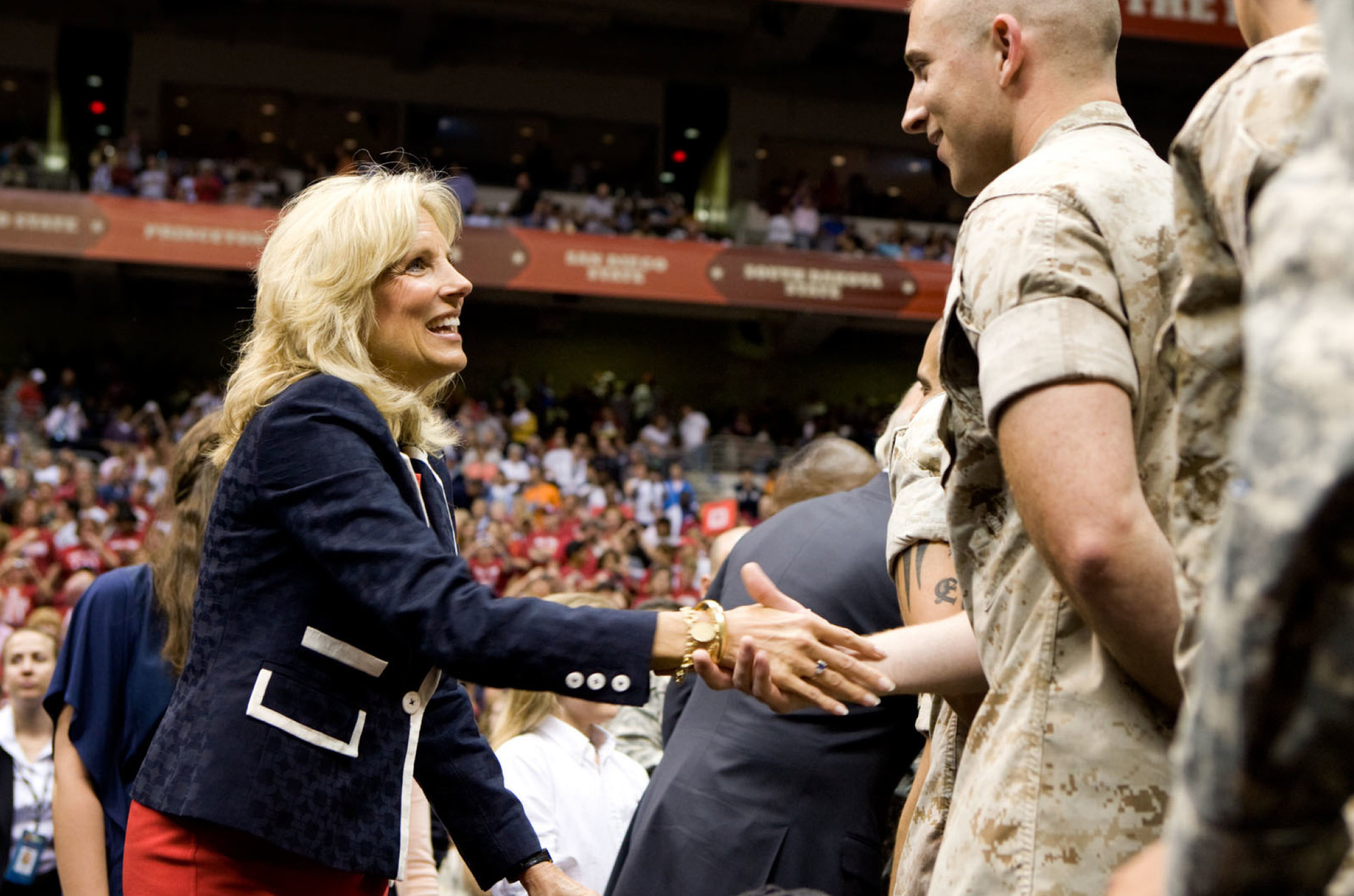 La Dra. Jill Biden luciendo un bléiser, dándole un apretón de manos a los miembros de las Fuerzas Armadas