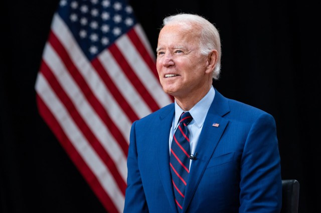 President Joe Biden wearing a suit, standing in front of an American flag
