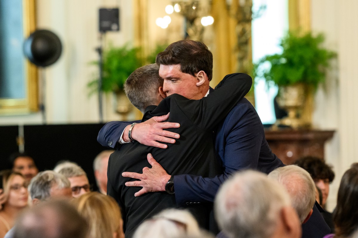 Kevin Jensen hugs Under Secretary for Memorial Affairs Samuel Brown as President Donald Trump delivers remarks at a National Purple Heart Day ceremony in the East Room, Thursday, August 7, 2025. (Official White House Photo by Joyce N. Boghosian)
